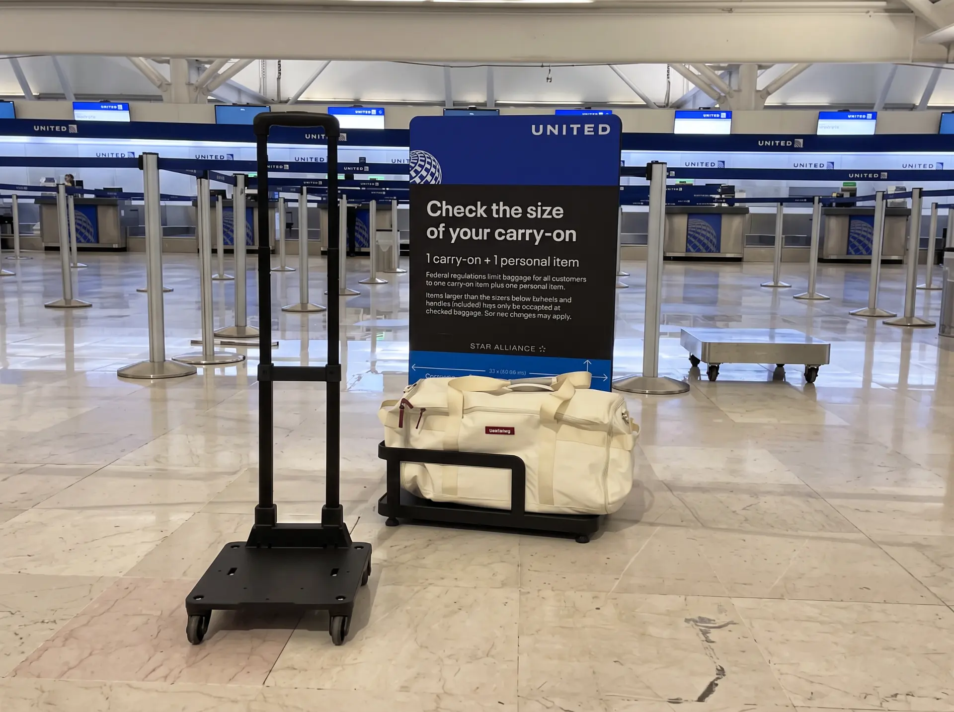 The cream Voyager bag beside an airline carry-on size checker at the airport