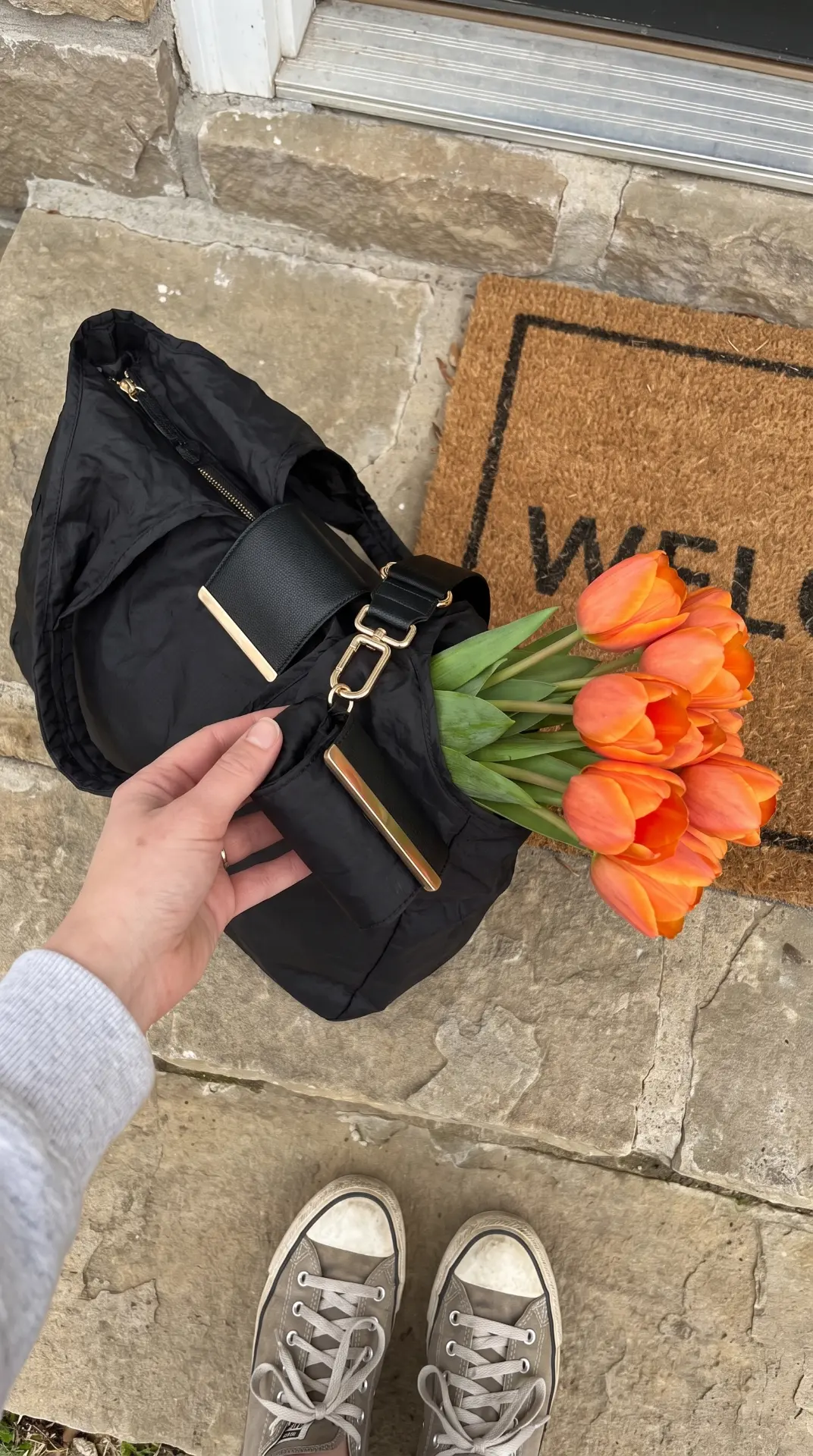Hand holding the cliptote by the door next to tulips, showing the gold clasp