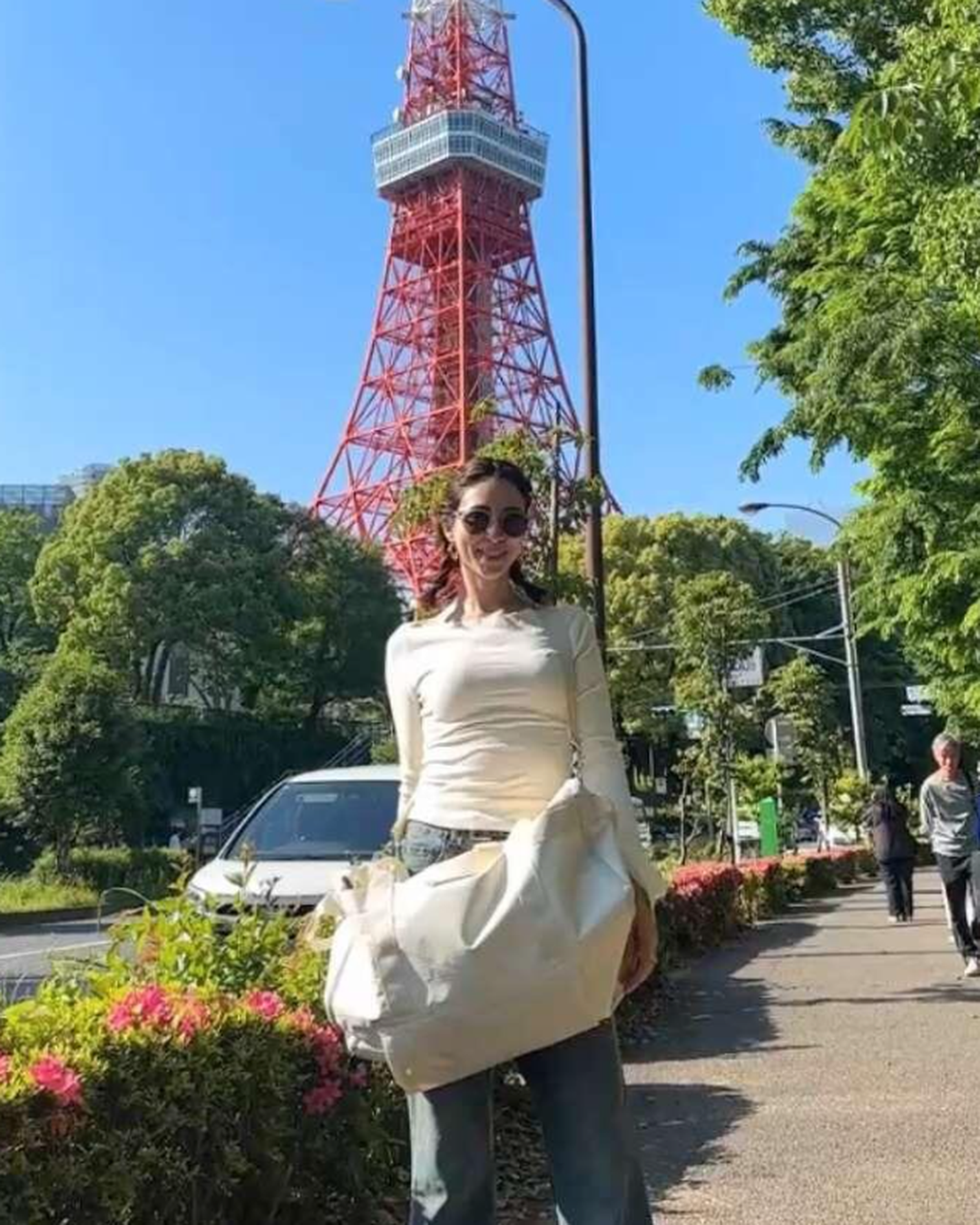 Woman carrying the cream Voyager bag on a street below Tokyo Tower